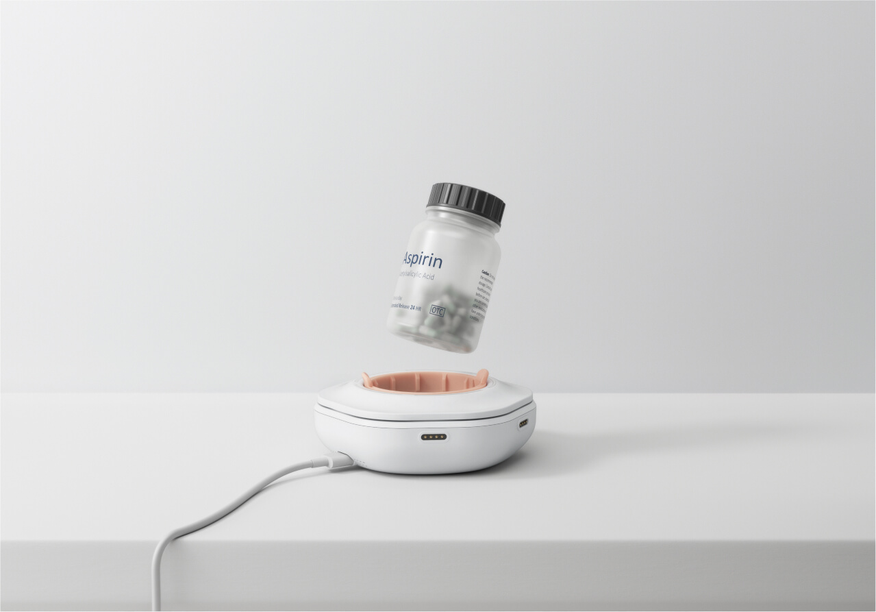 Ownum - The smart pill reminder device designed by Studio Copilot with an aspirin bottle suspended above its compartment, connected via a charging cable.