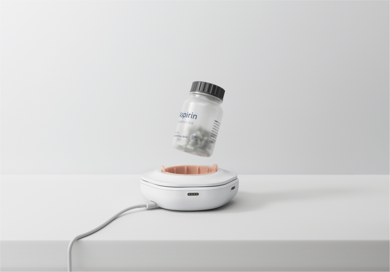 Ownum - The smart pill reminder device designed by Studio Copilot with an aspirin bottle suspended above its compartment, connected via a charging cable.