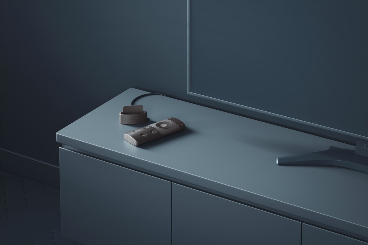 A sleek remote control placed next to its charging dock on a modern cabinet in a dark, minimalist setting.