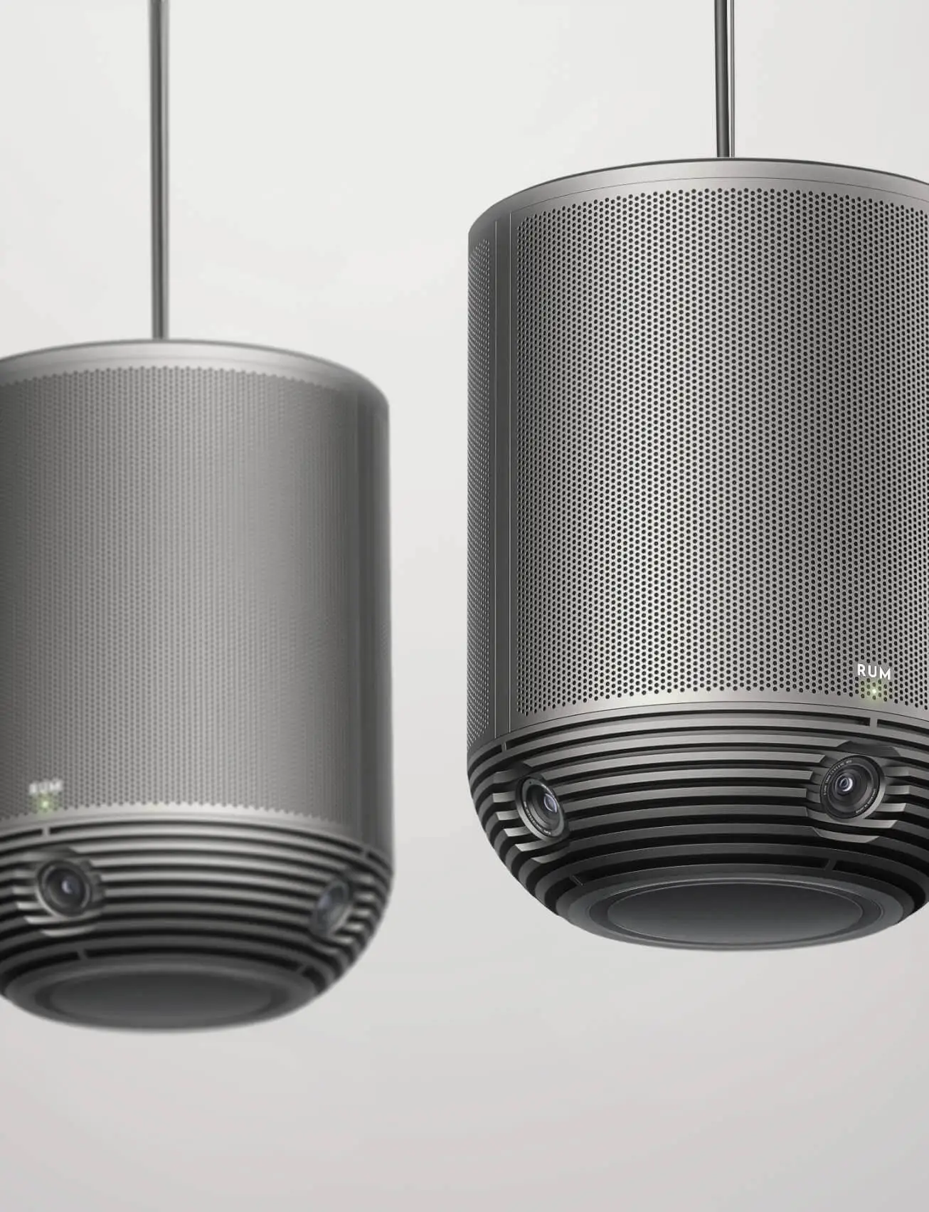 Two suspended RUM devices, designed by Studio Copilot, combining a Bluetooth speaker with integrated 360° cameras, featuring a sleek metallic design.
